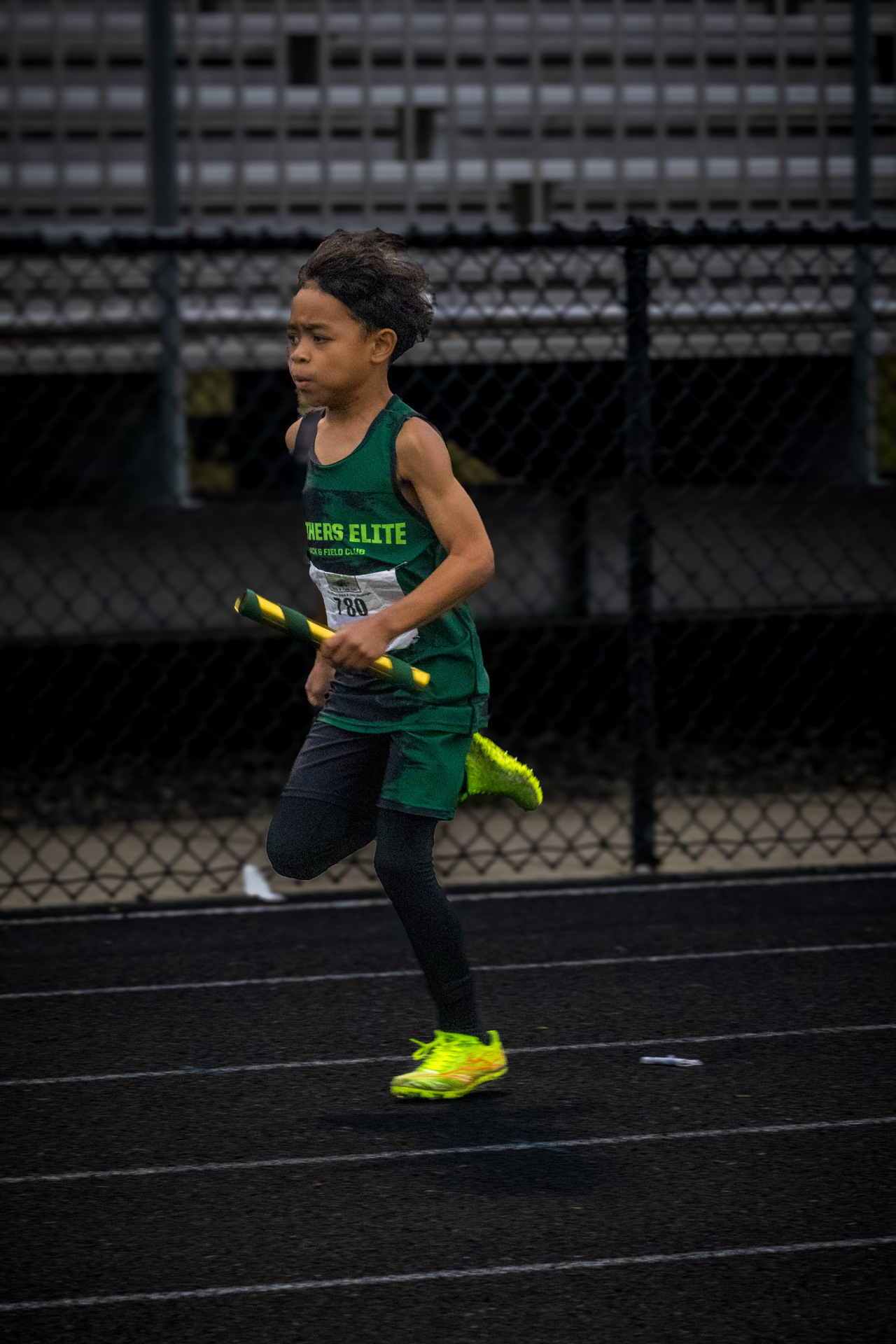 Young athlete running on track with relay baton at Panthers Elite Track & Field Club.
