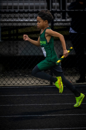 Young athlete running with a baton during a track and field event.