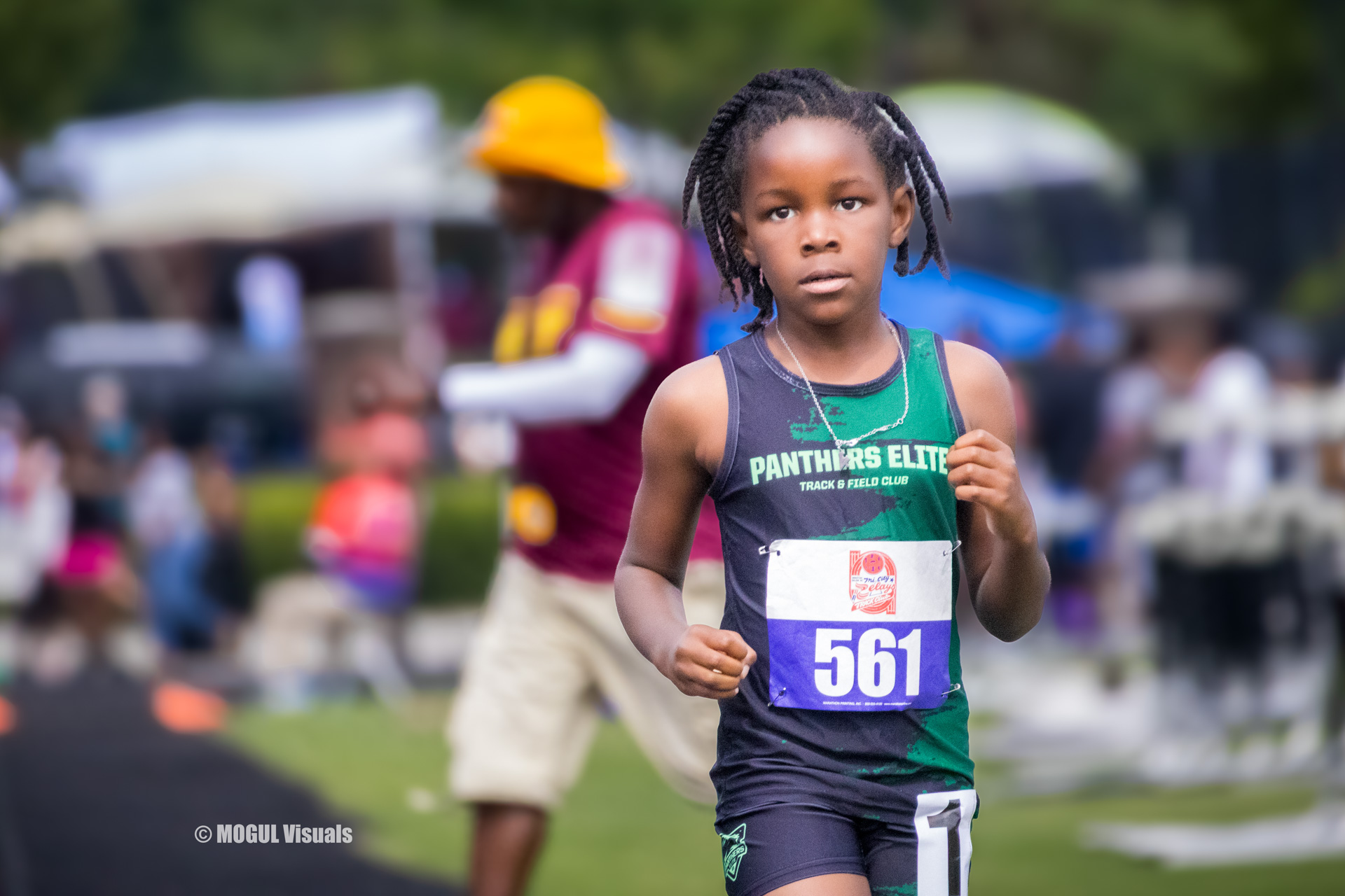 Young female athlete running at a track meet, wearing a Panthers Elite uniform with bib number 561.