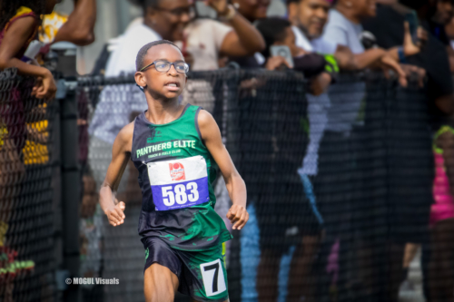 Young male runner wearing green Panthers Elite jersey during track race.