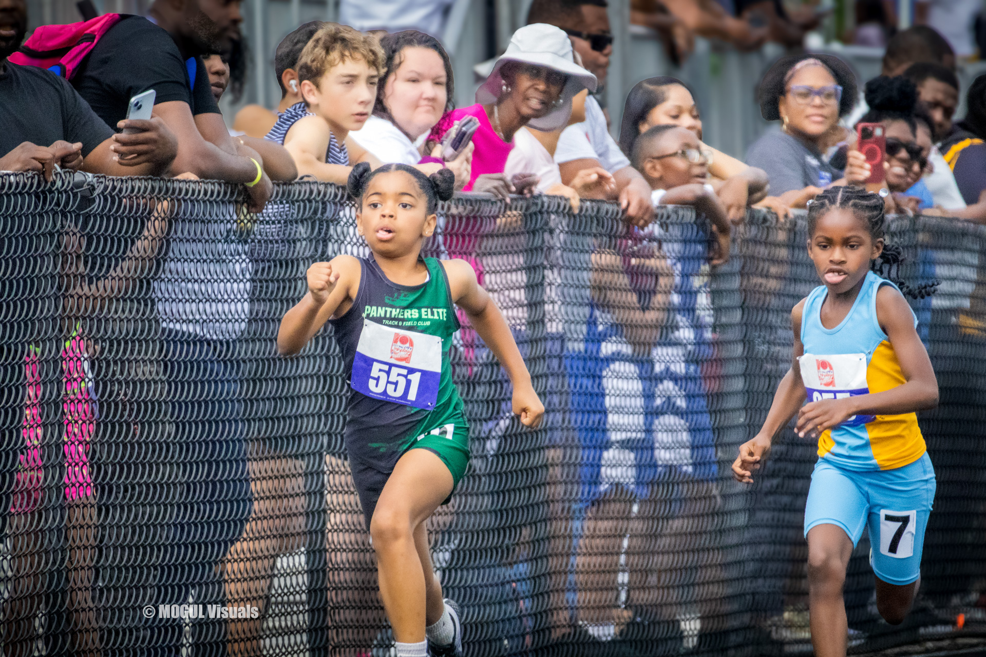 Young female athlete running in a track race with spectators cheering.