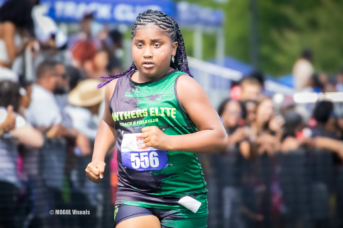 Young female athlete running in a race, wearing a green Panthers Elite uniform with bib number 556.