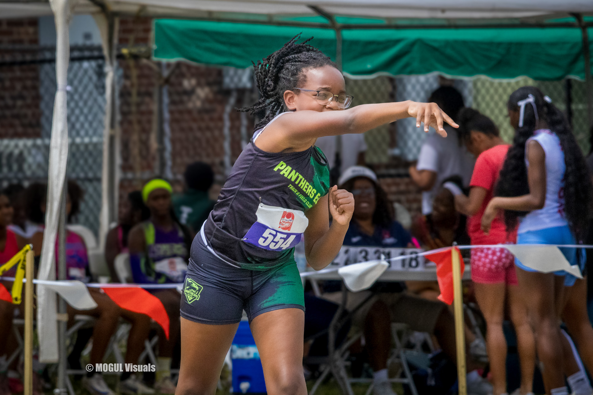 Athlete preparing to throw at a track meet, surrounded by teammates and spectators under a green ten.