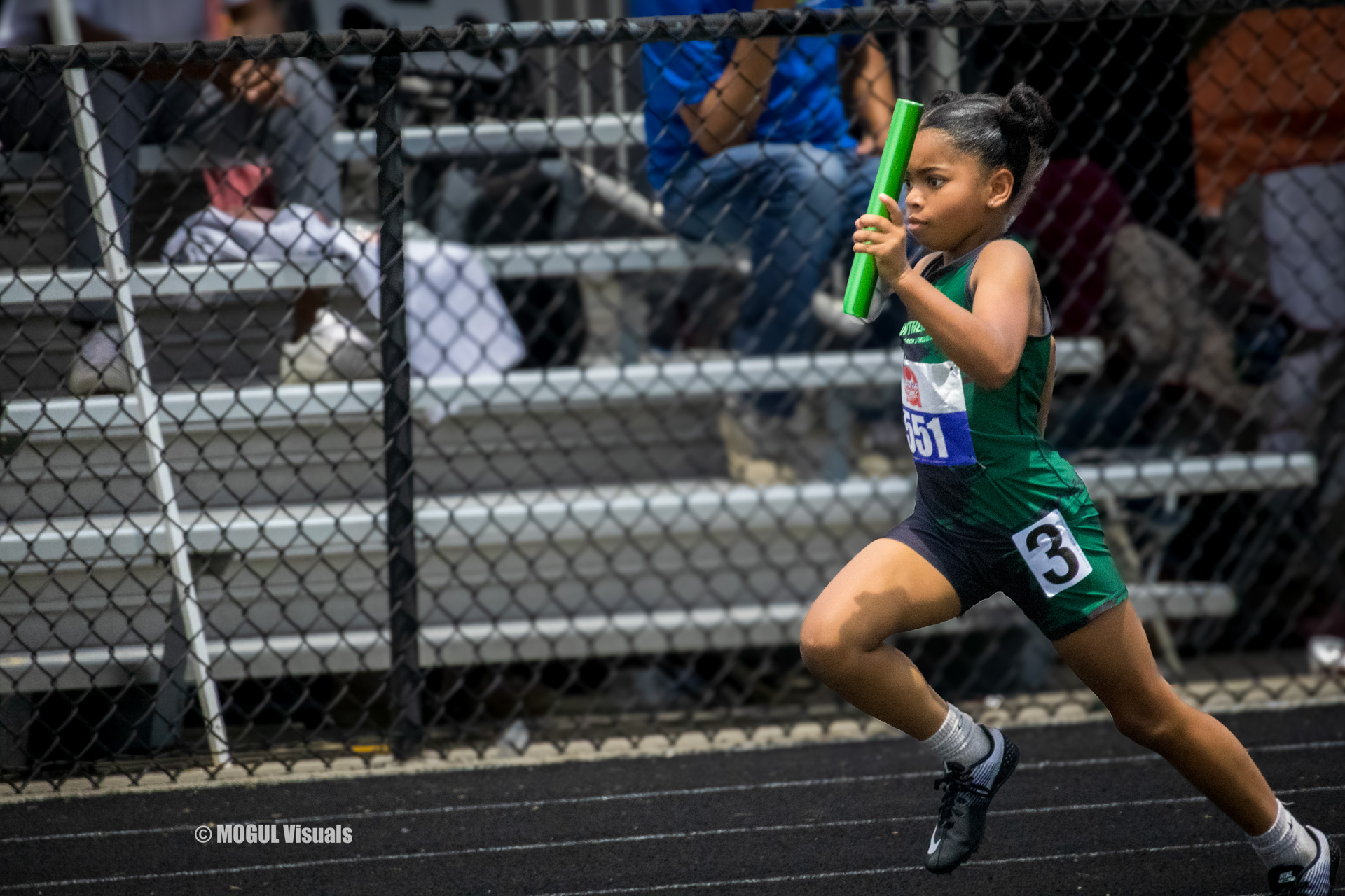 Young girl running with baton at track meet.