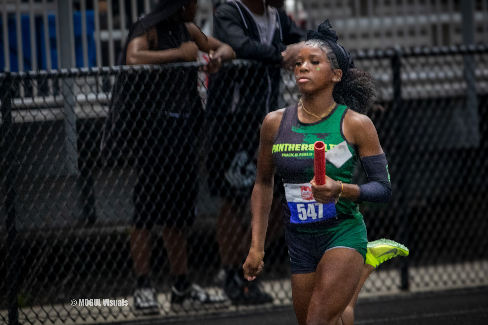 Female track athlete running with baton during a race at Panthers Elite Track & Field Club event.