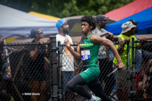 Young athlete running at a Panthers Elite Track & Field event behind a fence.