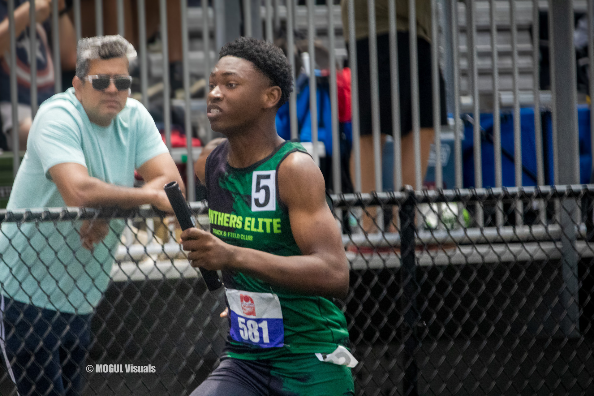 Athlete running with a baton during a relay race at a track meet.