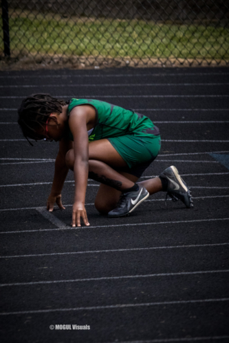 Young athlete crouching at the starting line on a track field.