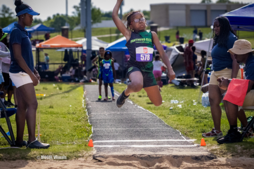 Young female athlete jumping long jump at a track meet.