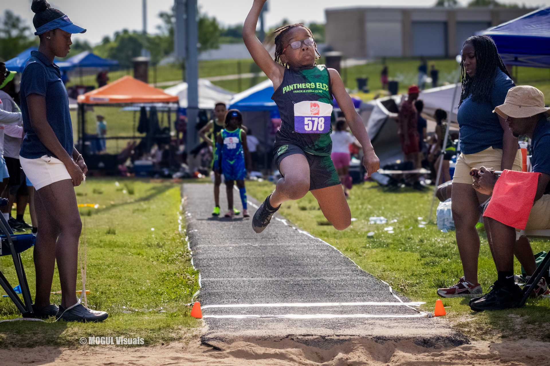 Young female athlete jumping long jump at a track meet.