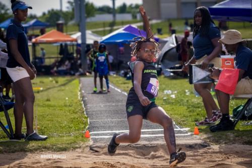 Young female athlete in mid-jump during a track and field event at Panthers Elite.
