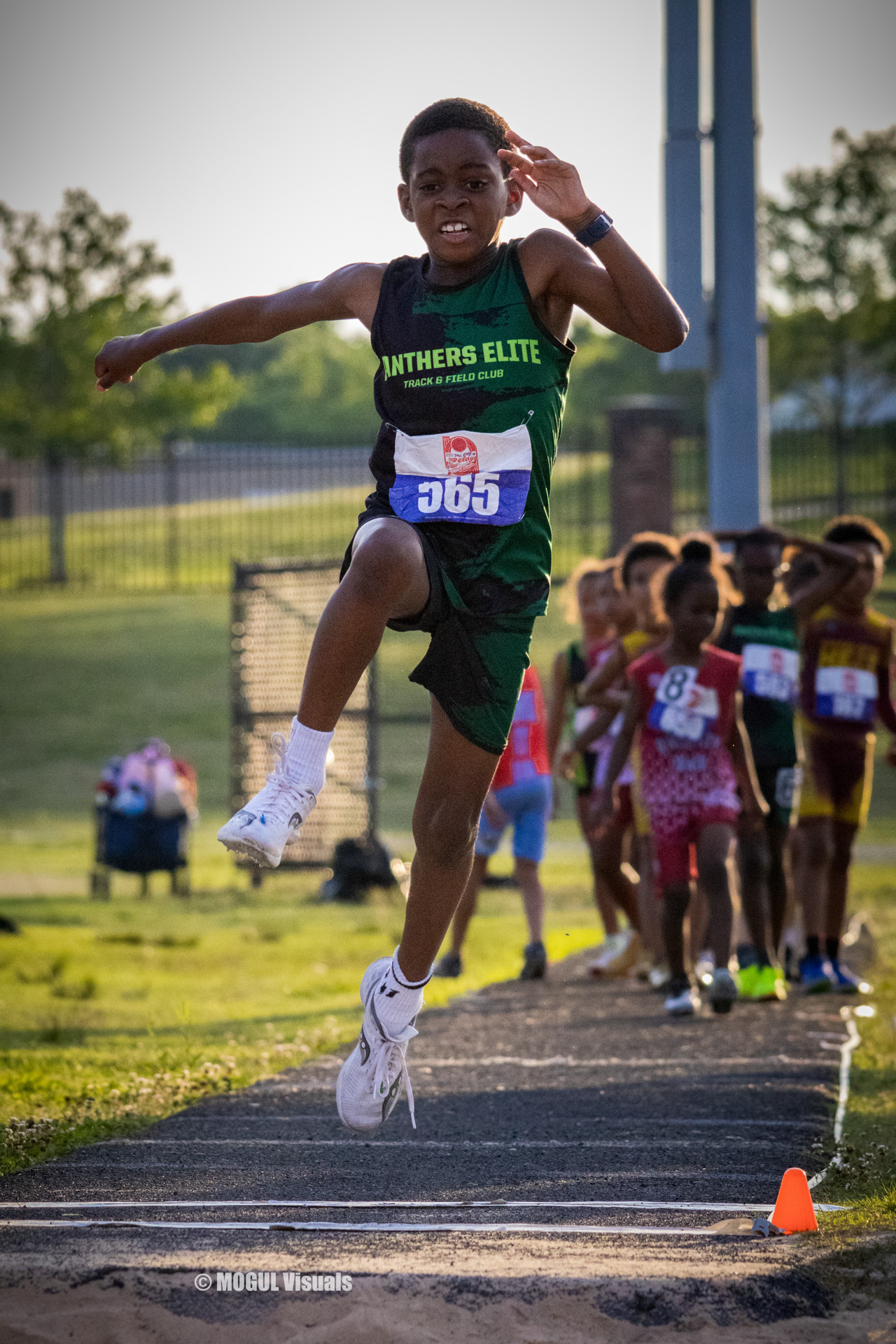 Young athlete in mid-air during a long jump event at a track meet.