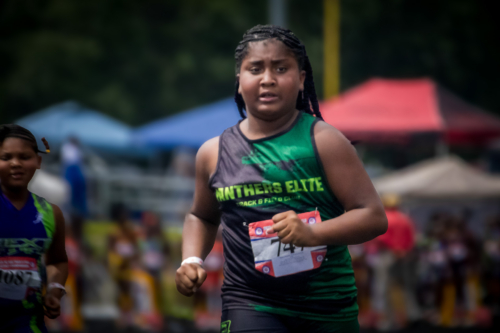 Young female athlete running at a track meet, Panthers Elite logo visible.