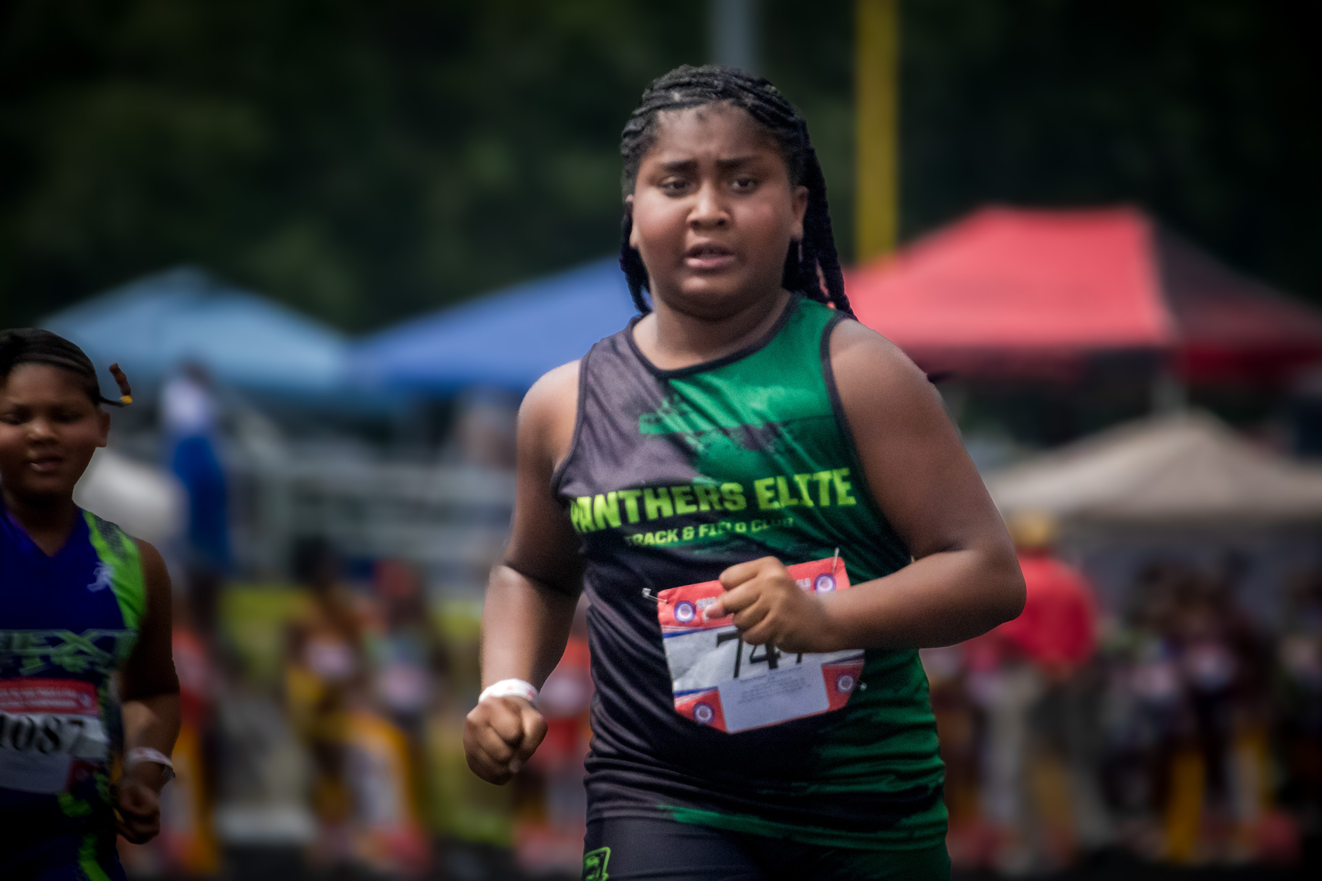 Young female athlete running at a track meet, Panthers Elite logo visible.