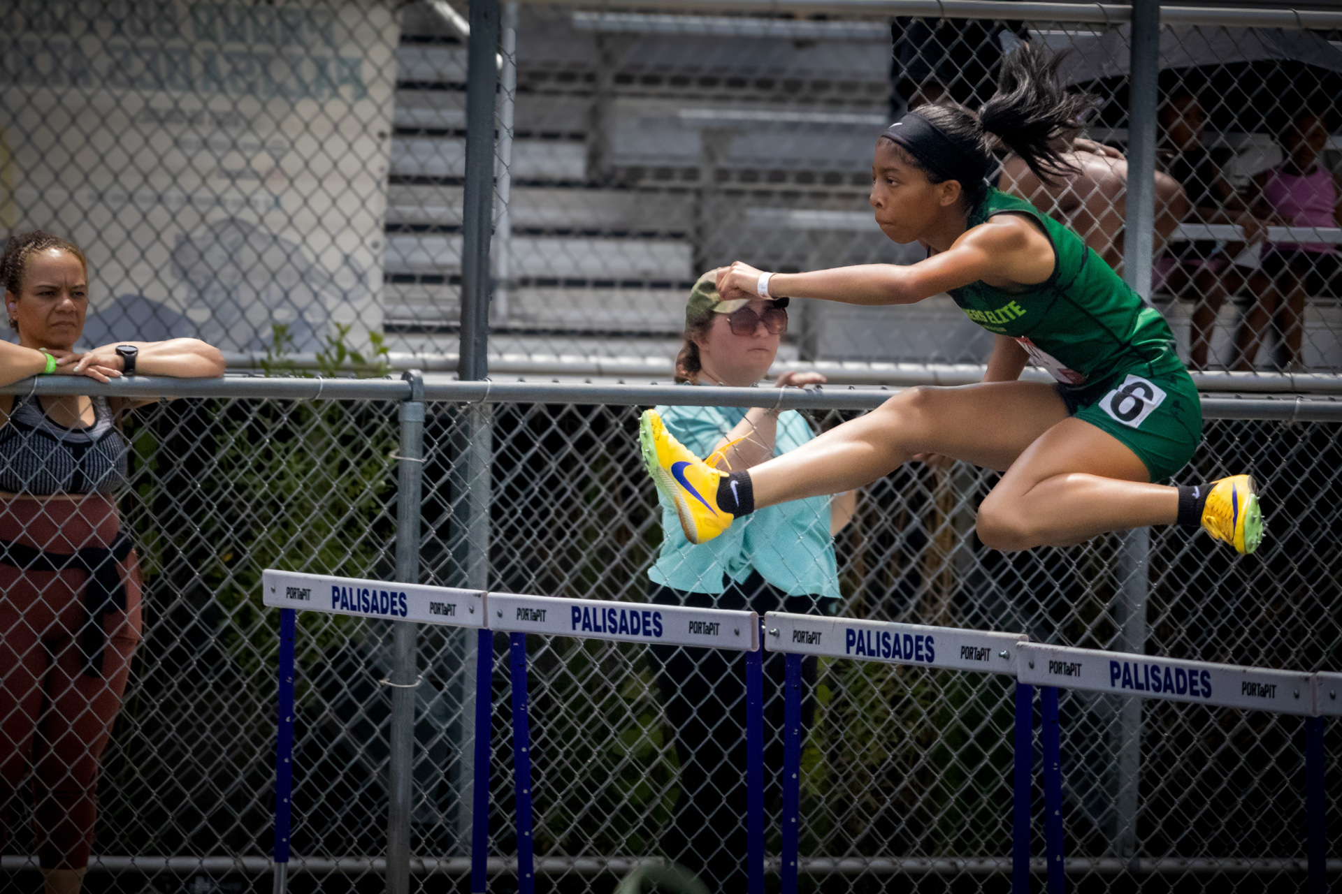 Female athlete jumping over hurdles at district qualifier meet.