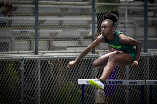 Female hurdler from Panthers Elite in mid-air at district qualifier.