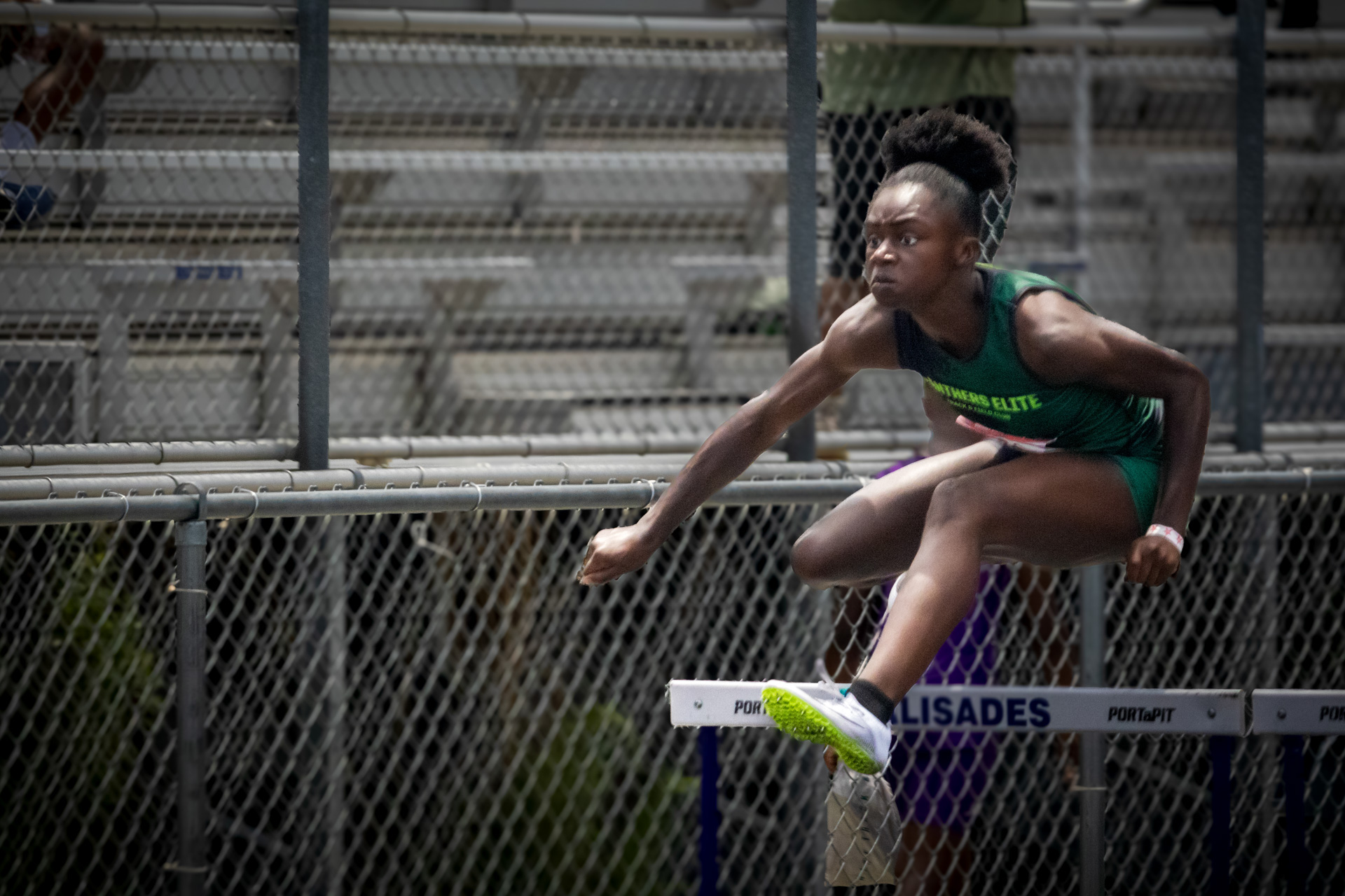 Female hurdler from Panthers Elite in mid-air at district qualifier.