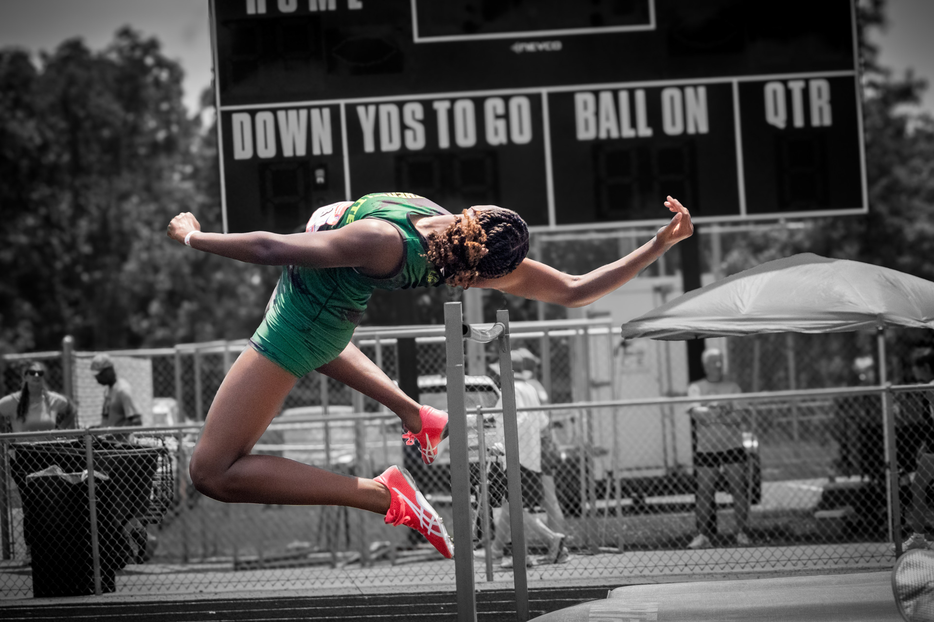Female track athlete jumping over hurdles at district qualifier event.