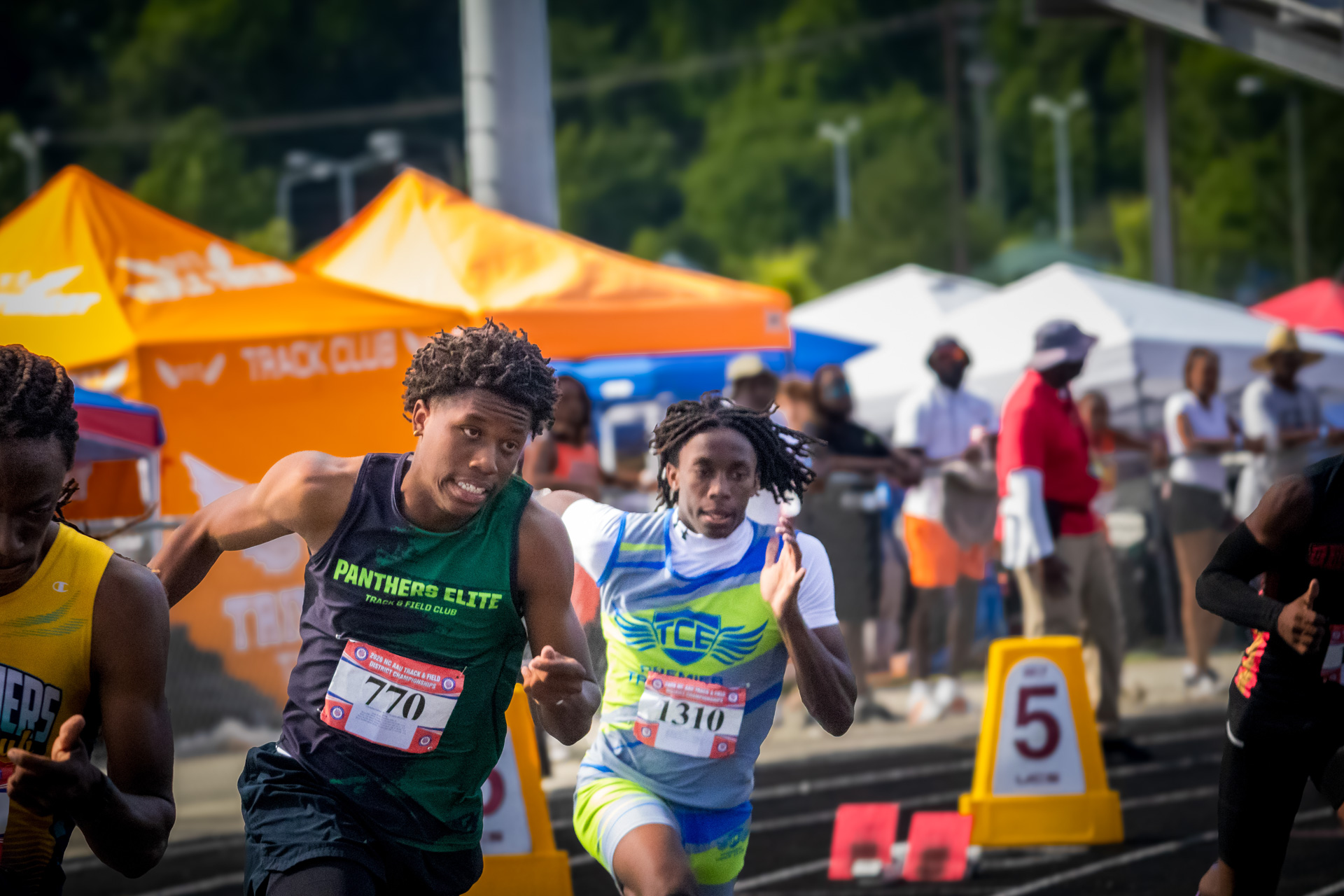 Panthers Elite runners competing at district track meet with spectators and tents in background.
