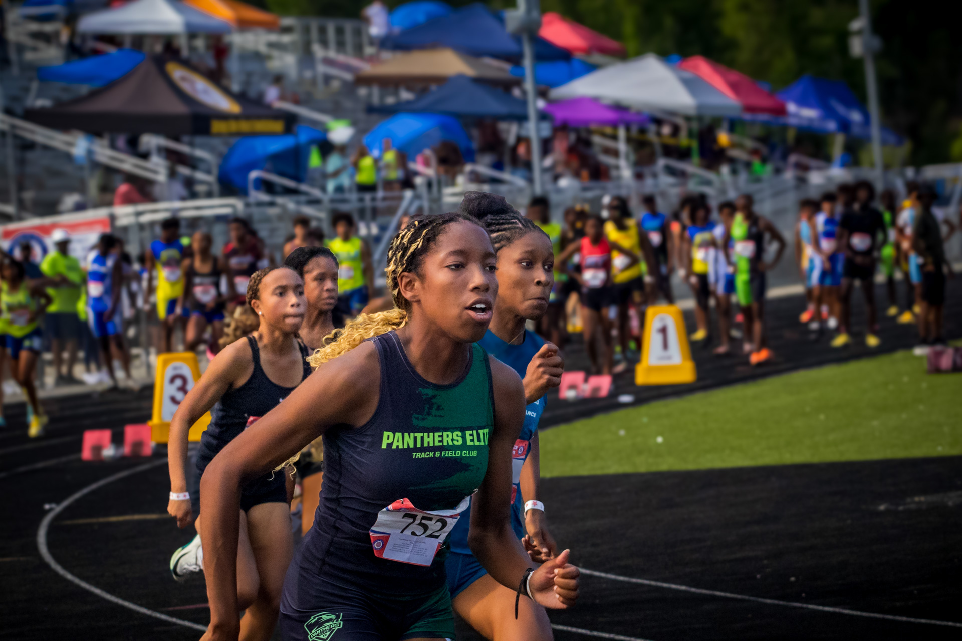 Panthers Elite athletes competing at district track meet with spectators and tents in background.