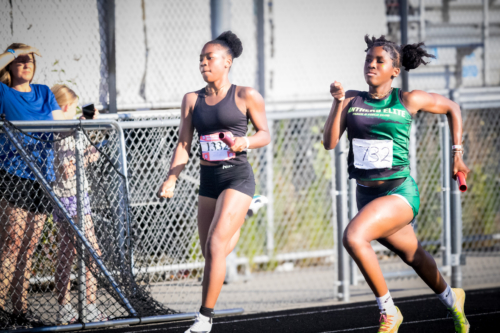 Two female athletes competing in a track race at a district qualifier event.