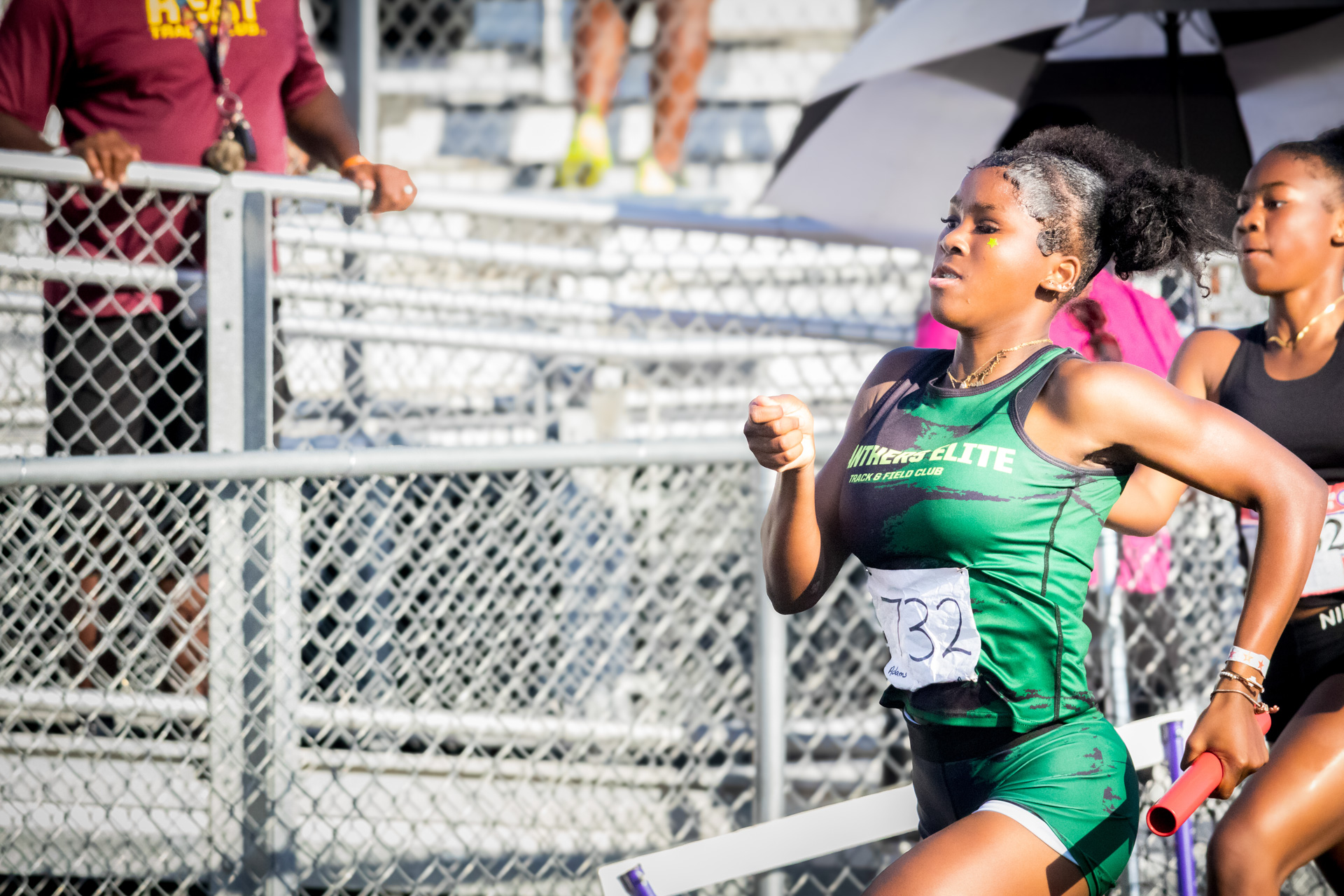 Female sprinter running at District Qualifier event with spectators in background.