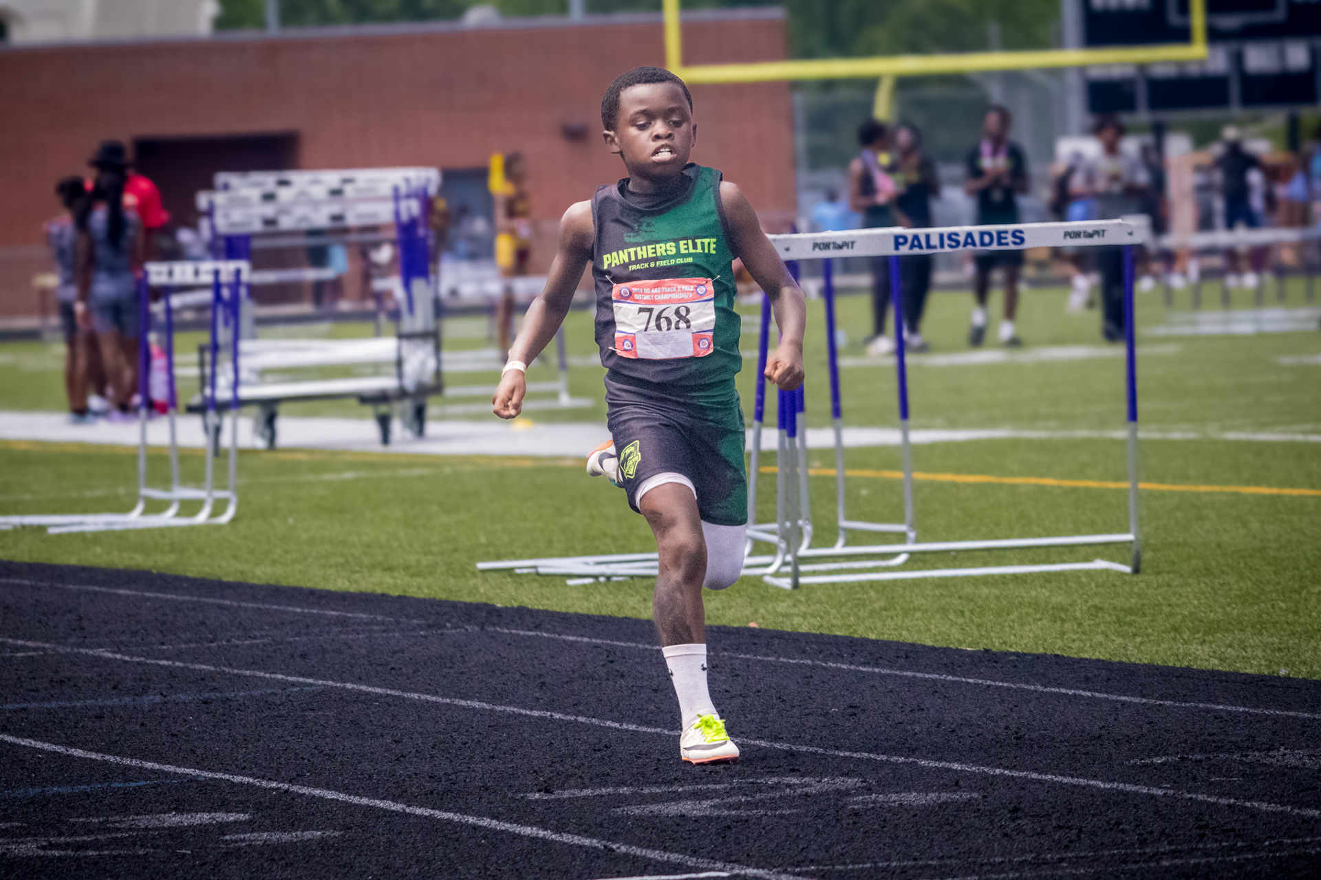 Young athlete competing in hurdles at district qualifier event.