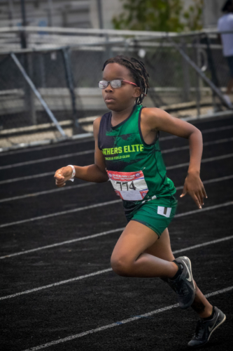 Young female athlete running on track at District Qualifier 2026.