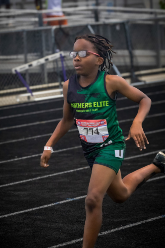 Young female athlete running on track at District Qualifier 2026.