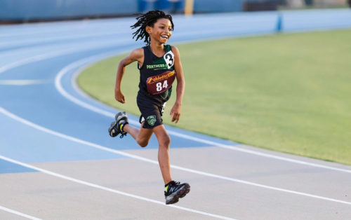 Young female athlete running on a track during a competition.