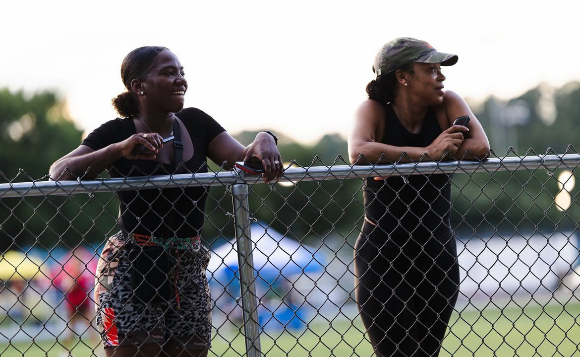 Two coaches watching a track meet behind a fence at The Victory Lap 2026.